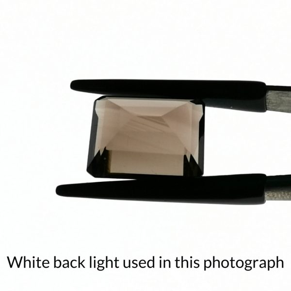 The brown smoky quartz rectangle gem is being back-lit with a bright white light to show any inclusions within the gem more clearly.