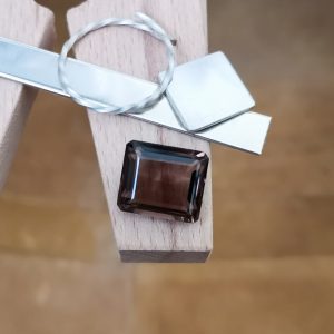 The dark brown smoky quartz rectangle displayed on a jewellers bench peg with some sterling silver sheet and wire.