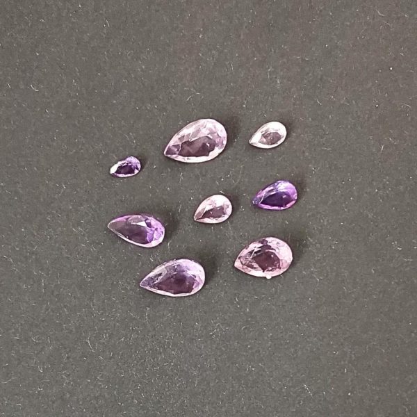 A photo of the 8 purple amethyst teardrops displayed on a black background showing they are in different shades of purple.