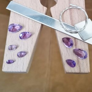 The bundle of purple amethyst teardrops displayed on a jewellers bench peg with some sterling silver sheet and wire.