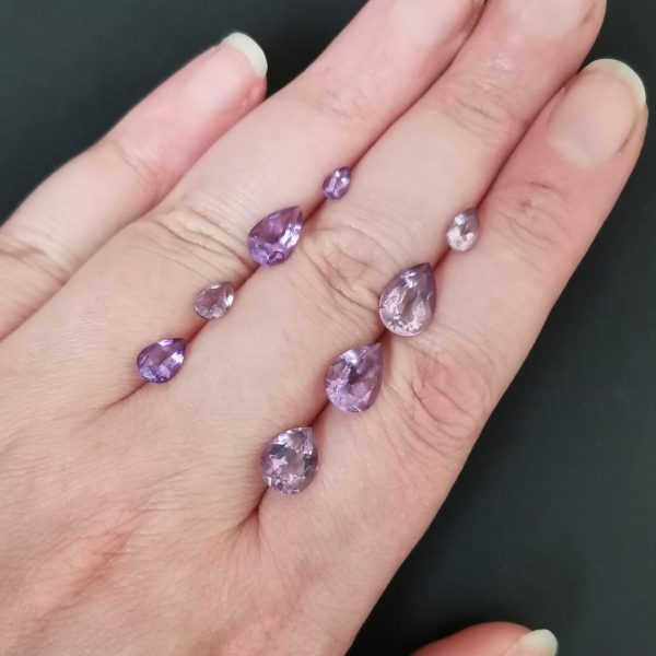 The 8 purple amethyst gemstones resting on a hand to give an idea of the gemstones size and colour.