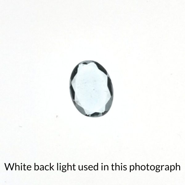 The pale blue aquamarine oval gem is being back-lit with a bright white light to show any inclusions within the gem more clearly.