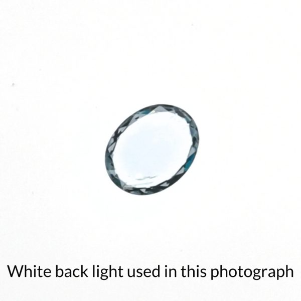 The pale blue aquamarine oval gem is being back-lit with a bright white light to show any inclusions within the gem more clearly.