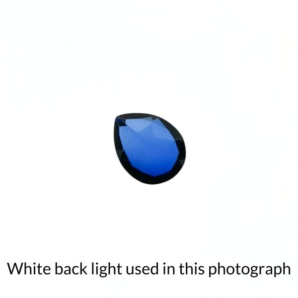The bright blue lab grown sapphire teardrop gem is being back-lit with a bright white light to show any inclusions within the gem more clearly.