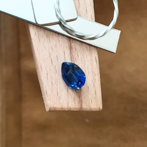 The lab grown blue sapphire teardrop displayed on a jewellers bench peg with some sterling silver sheet and wire.