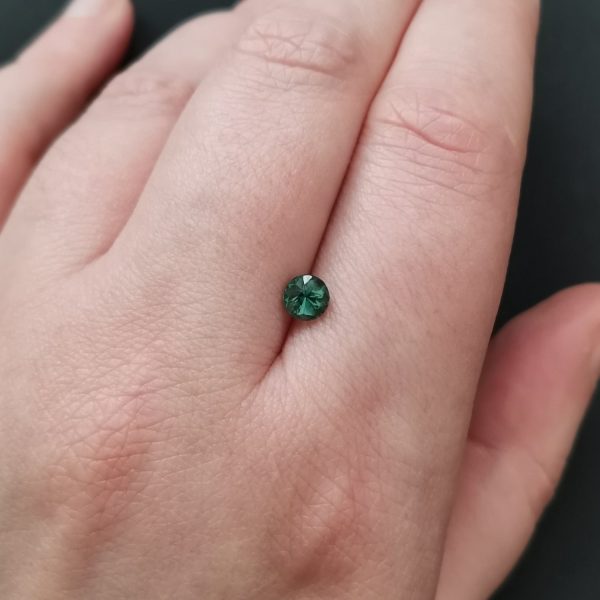 The dark green tourmaline gemstone resting on a hand to give an idea of the gemstones size and colour.