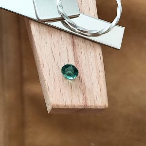 The green tourmaline round displayed on a jewellers bench peg with some sterling silver sheet and wire.