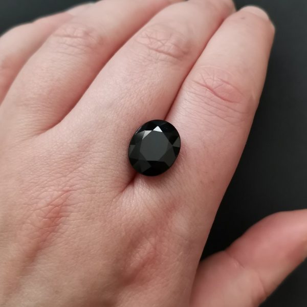 The large black sapphire gemstone resting on a hand to give an idea of the gemstones size and colour.