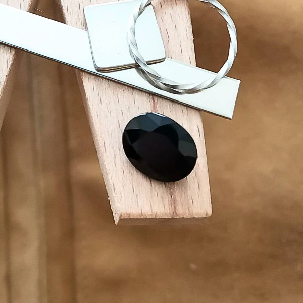 The black sapphire oval displayed on a jewellers bench peg with some sterling silver sheet and wire.
