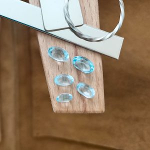 The bundle of sky blue topaz ovals displayed on a jewellers bench peg with some sterling silver sheet and wire.