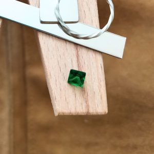 The green tsavorite garnet square displayed on a jewellers bench peg with some sterling silver sheet and wire.