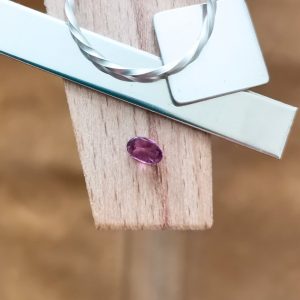 The purplish pink sapphire oval displayed on a jewellers bench peg with some sterling silver sheet and wire.