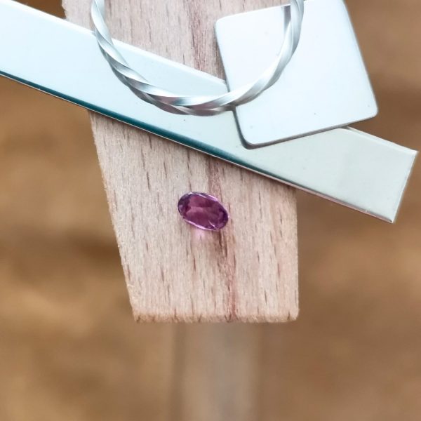 The purplish pink sapphire oval displayed on a jewellers bench peg with some sterling silver sheet and wire.