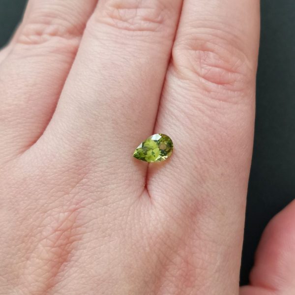 The green peridot gemstone resting on a hand to give an idea of the gemstones size and colour.
