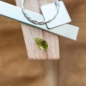 The green peridot teardrop displayed on a jewellers bench peg with some sterling silver sheet and wire.