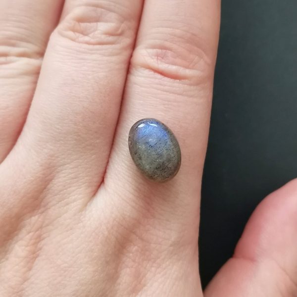 The grey labradorite gemstone resting on a hand to give an idea of the gemstones size and colour.