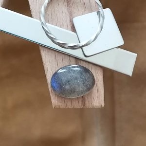 The oval labradorite cabochon displayed on a jewellers bench peg with some sterling silver sheet and wire.