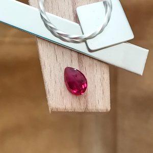 The lab grown ruby teardrop displayed on a jewellers bench peg with some sterling silver sheet and wire.