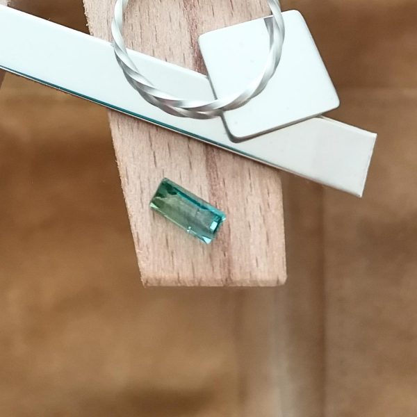 The two tone tourmaline rectangle displayed on a jewellers bench peg with some sterling silver sheet and wire.