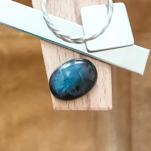 The oval labradorite cabochon displayed on a jewellers bench peg with some sterling silver sheet and wire.