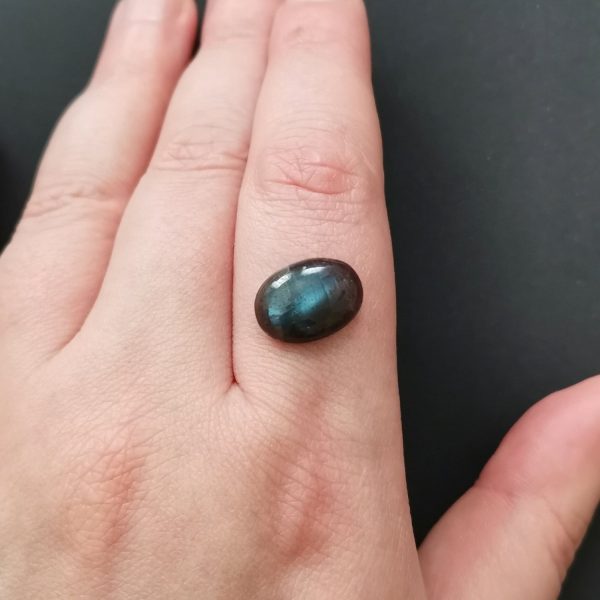 The dark labradorite gemstone resting on a hand to give an idea of the gemstones size and colour.