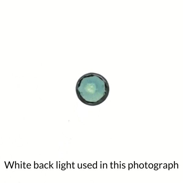 The small round sapphire gem is being back-lit with a bright white light to show any inclusions within the gem more clearly.