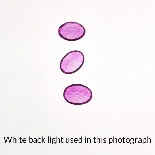 The colour coated oval topaz gems is being back-lit with a bright white light to show any inclusions within the gems more clearly.