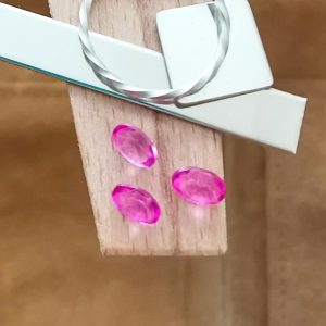 The colour coated pink topaz ovals displayed on a jewellers bench peg with some sterling silver sheet and wire.
