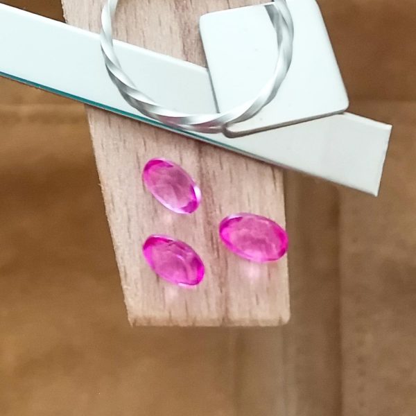 The colour coated pink topaz ovals displayed on a jewellers bench peg with some sterling silver sheet and wire.