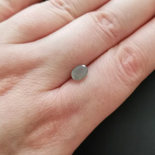 The grey moonstone gemstone resting on a hand to give an idea of the gemstones size and colour.