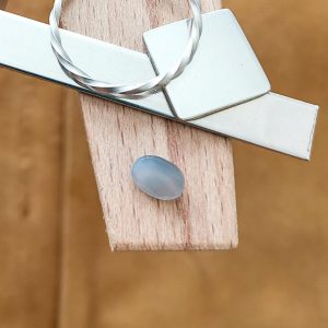 The grey moonstone oval displayed on a jewellers bench peg with some sterling silver sheet and wire.