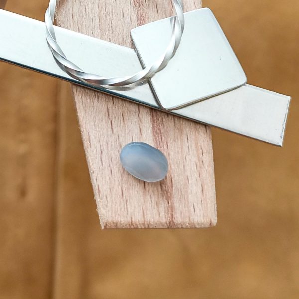 The grey moonstone oval displayed on a jewellers bench peg with some sterling silver sheet and wire.