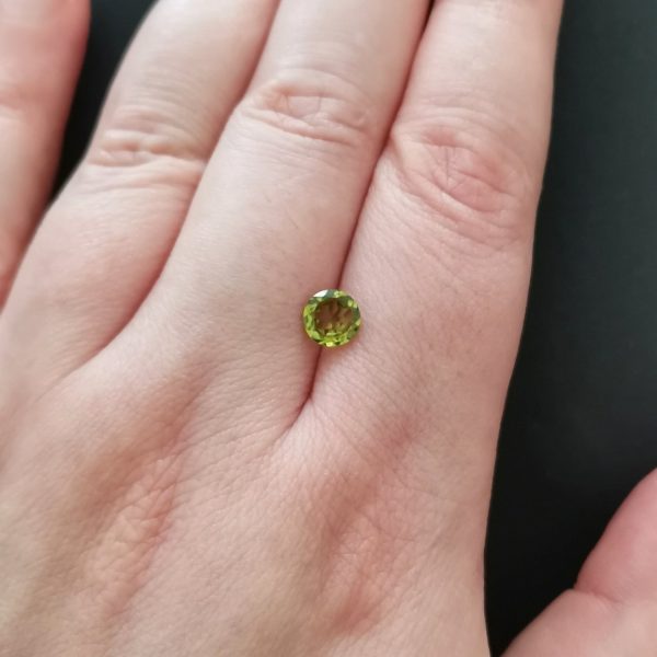 The green peridot gemstone resting on a hand to give an idea of the gemstones size and colour.
