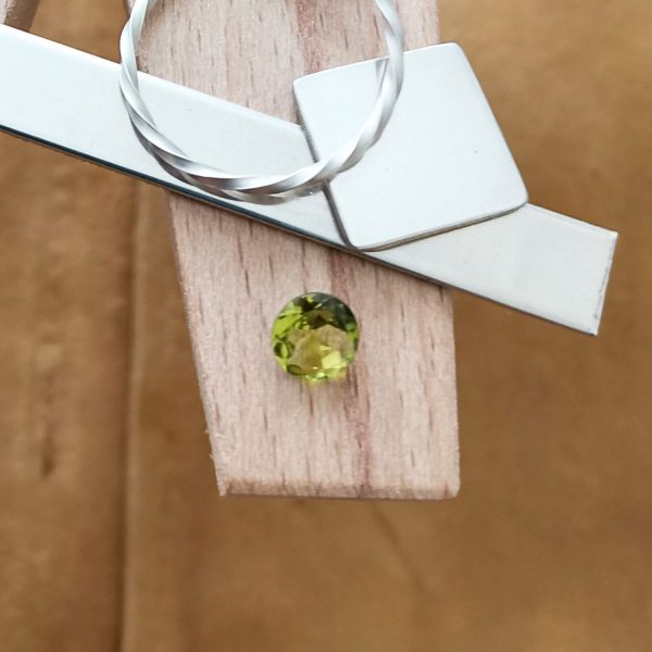 The green peridot round displayed on a jewellers bench peg with some sterling silver sheet and wire.
