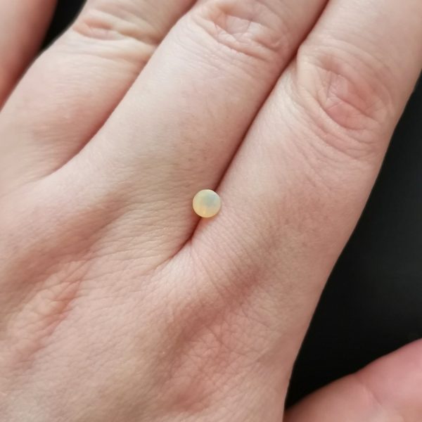 The small opal gemstone resting on a hand to give an idea of the gemstones size and colour.