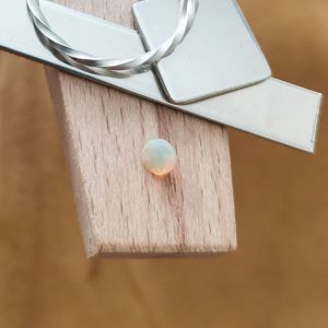 The round opal displayed on a jewellers bench peg with some sterling silver sheet and wire.