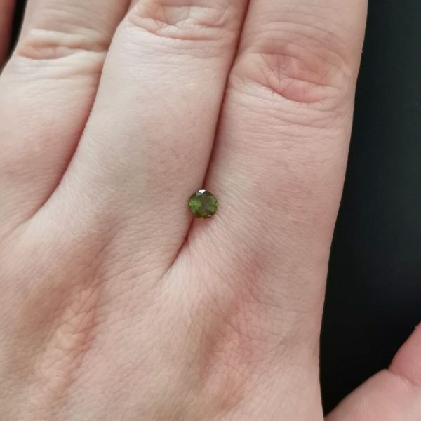 The green tourmaline gemstone resting on a hand to give an idea of the gemstones size and colour.