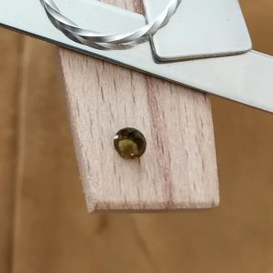 The green tourmaline round displayed on a jewellers bench peg with some sterling silver sheet and wire.