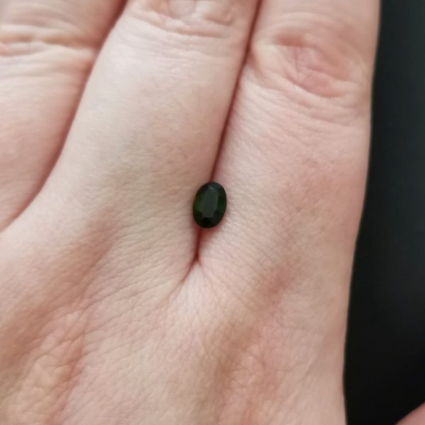 The dark green tourmaline gemstone resting on a hand to give an idea of the gemstones size and colour.