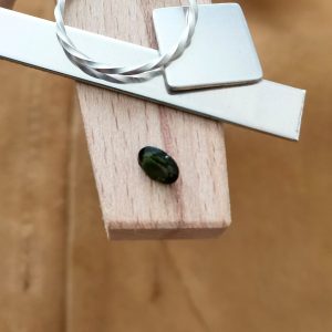 The green tourmaline oval displayed on a jewellers bench peg with some sterling silver sheet and wire.