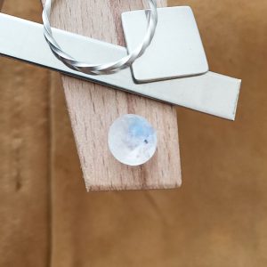 The round white moonstone displayed on a jewellers bench peg with some sterling silver sheet and wire.