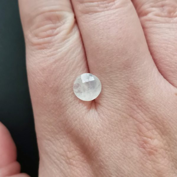 The white moonstone gemstone resting on a hand to give an idea of the gemstones size and colour.