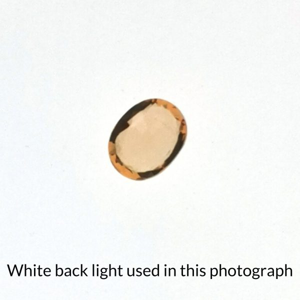 The oval shaped sapphire gem is being back-lit with a bright white light to show any inclusions within the gem more clearly.