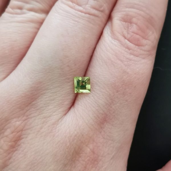 The green peridot gemstone resting on a hand to give an idea of the gemstones size and colour.