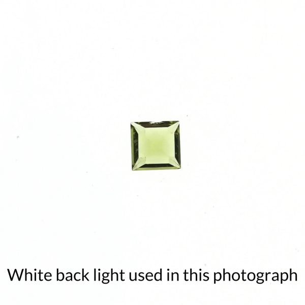 The square shaped peridot gem is being back-lit with a bright white light to show any inclusions within the gem more clearly.