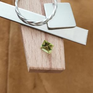 The green peridot square displayed on a jewellers bench peg with some sterling silver sheet and wire.