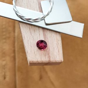 The dark pink tourmaline displayed on a jewellers bench peg with some sterling silver sheet and wire.