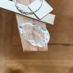 The large clear quartz teardrop displayed on a jewellers bench peg with some sterling silver sheet and wire.
