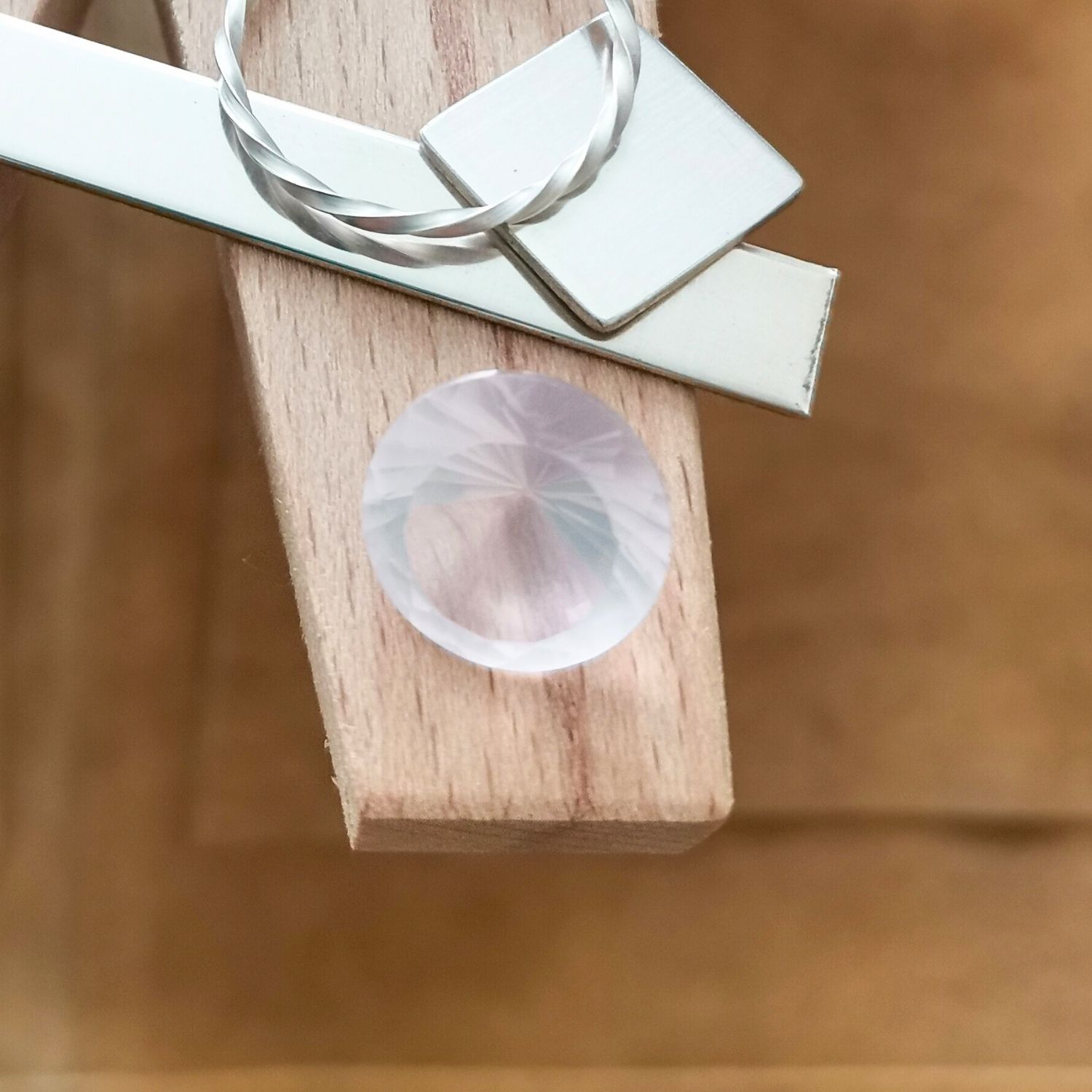 The faceted round rose quartz displayed on a jewellers bench peg with some sterling silver sheet and wire.