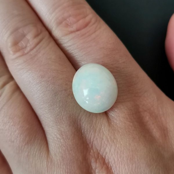 The white opal gemstone resting on a hand to give an idea of the gemstones size and colour.
